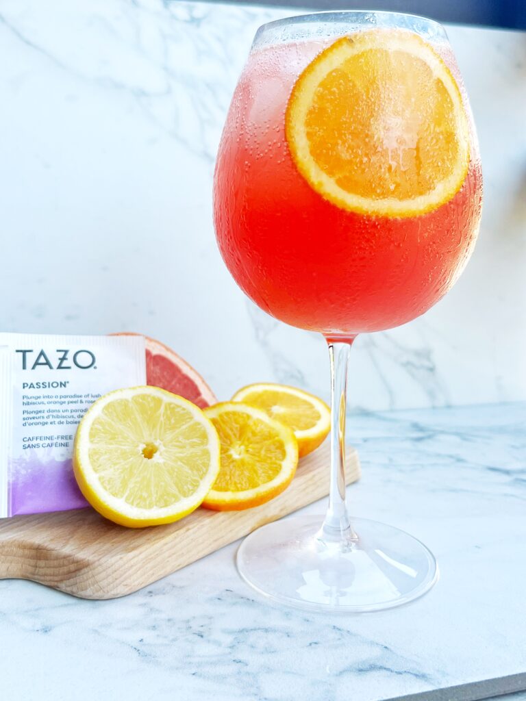 Bright and refreshing Passion Spritz served in a glass with ice and citrus slices, featuring passion tea, orange juice, and sparkling water for a summer drink