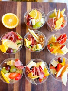 Simple Charcuterie Cups filled with fresh fruit, cheese cubes, salami slices, and pretzels, arranged in clear cups on a serving tray for a party.