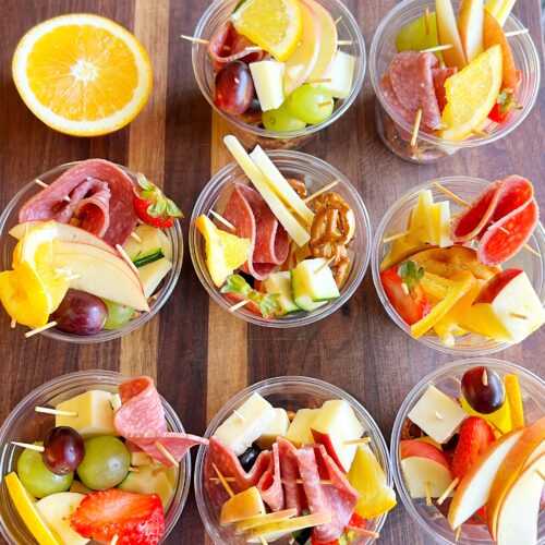 Simple Charcuterie Cups filled with fresh fruit, cheese cubes, salami slices, and pretzels, arranged in clear cups on a serving tray for a party.